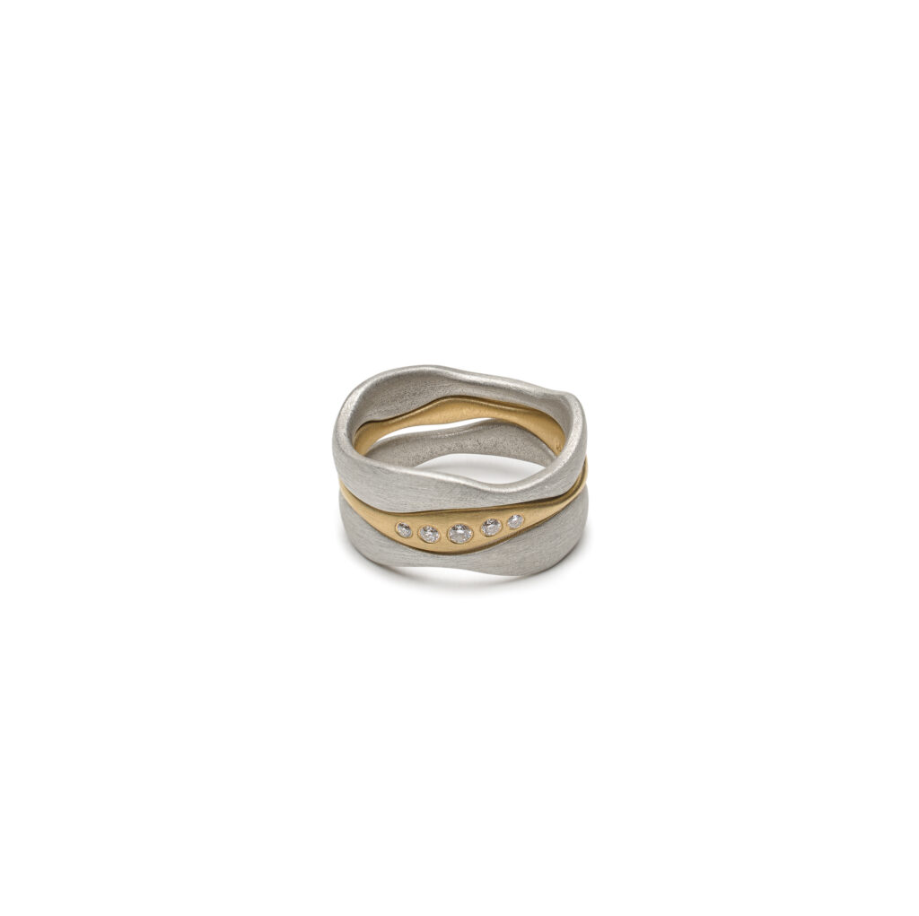 Lirien ring set with two sterling silver bands and one 14K gold band featuring five flush-set diamonds and flowing shapes.